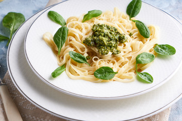 Appetizing pasta with sauce pesto and spinach in plate on light blue stone table.