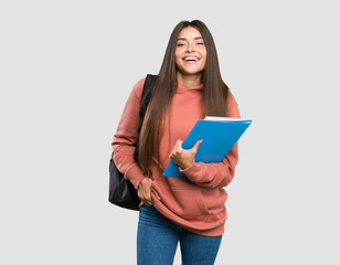 Young student woman holding notebooks laughing over isolated grey background
