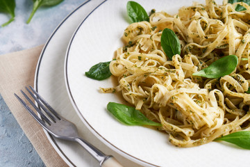 Appetizing pasta with sauce pesto and spinach in plate on light blue stone table.