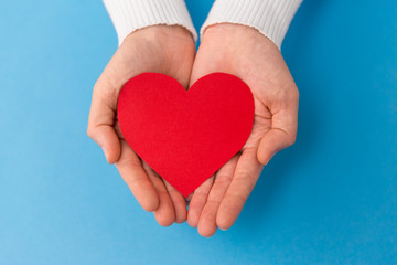 Obraz premium love, health and valentine's day concept - hands holding red heart shape on blue background