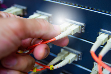 Technician connect fiber cable network to switch port in server room , Concept internet network management