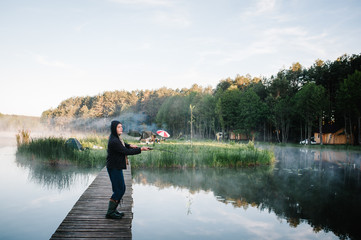 Fisherman with fishing rod on bridge. Sunrise. Fishing for pike, perch, carp. Fog, grass, trees against the backdrop of lakes, nature. Fishing background. Misty morning. the wild nature. river