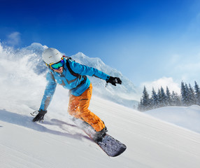 Young man snowboarder running down the slope in Alpine mountains - obrazy, fototapety, plakaty