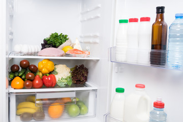 vegetables and fruits lie inside a white open refrigerator