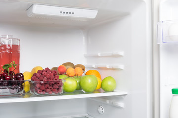 fruits, berries and a drink lie inside a white open refrigerator