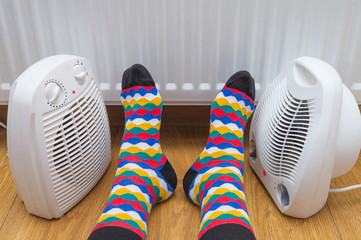 Feet wearing bright multi colored socks near heaters at home. The symbolic image of a house heating...