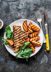 Pork chop with caramelized grilled apples and arugula salad on a dark background, top view