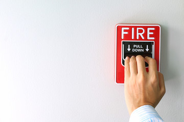 Hand of woman pulling fire alarm switch on the white wall as background for emergency case at the office
