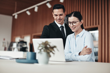 Smiling businesspeople standing in an office working on a laptop