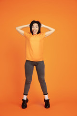 Caucasian young woman's portrait on orange studio background. Beautiful female brunette model in shirt. Concept of human emotions, facial expression, sales, ad. Copyspace. Winning, crazy happy.