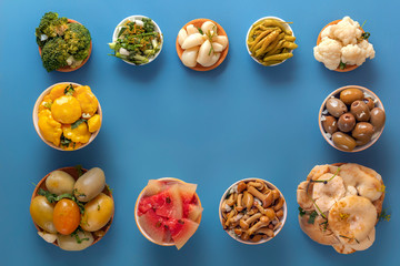 Fermented products cabbage, peppers, pickles, tomatoes, mushrooms, zucchini, garlic on a blue table. Top view. Copy space