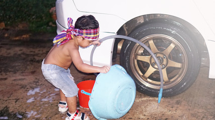 Happy Asian little boy 2 year old playing water from hose and spray to washing the car at outdoor in morning time. Kid and family activity concept.