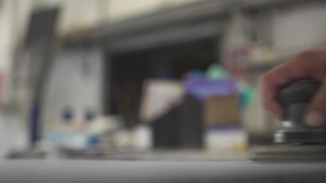 Close up of a metal worker sanding down a thin sheet of metal. View from inside the workshop. Slow motion.