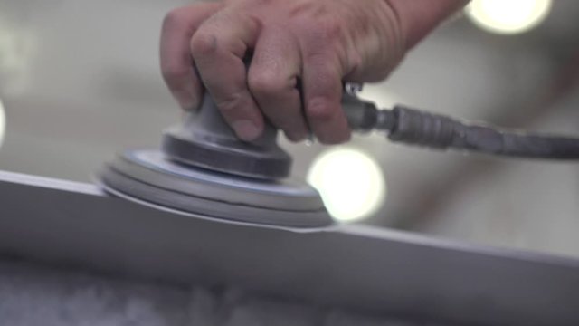 Close up of a worker using a small orbital sander to smooth out the edges of a silver metal sheet. Slow motion.