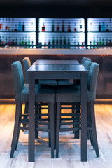Black wooden bar table with chairs in the pub with bottles at the background