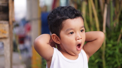 Asian boy sitting near the water front, pretending to be sleepy and yawning with a wide mouth.                              