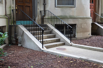 Walkway and concrete steps entryway to a brownstone apartment building with wrought iron railings, horizontal aspect