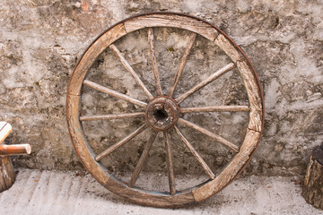 Fototapeta na wymiar An old wooden cart wheel against a stone fence.