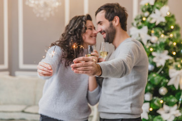 Concept of parties and entertainment. Sweet photo of energetic couple celebrating, with champange in lovely new year decorated room.