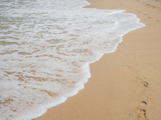 Wave with white foam rolls onto the sand of a beach