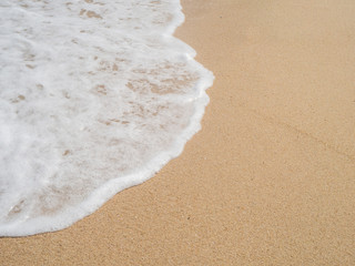 Wave with white foam rolls onto the sand of a beach