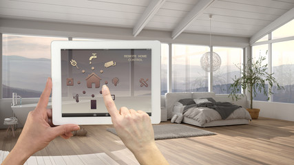 Smart remote home control system on a digital tablet. Device with app icons. Minimalist modern bright bedroom with bathtub in the background, architecture interior design