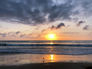 Colorful ocean beach sunset facing the sun with deep clouded sky. Beautiful cloudscape over the sea during sunset. 