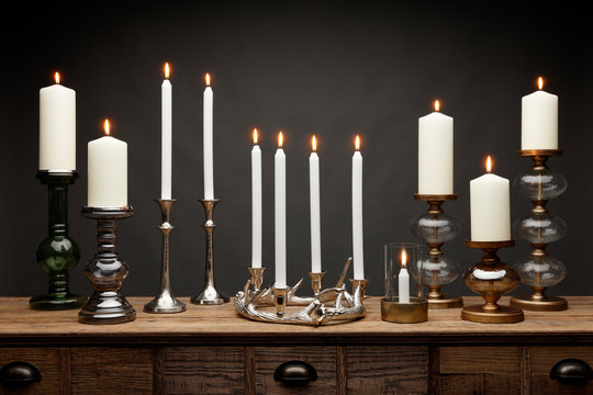A group of candle sticks and glowing candles, shot on a wooden table, with a dark grey background