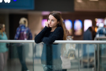 Teenager. Young pretty white caucasian teenage girl with long hair with problem skin and long hair in a shopping center near the railing.