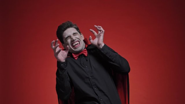 Terrified man dracula with fangs in black halloween costume becoming scared of light isolated over red wall                                                                                  