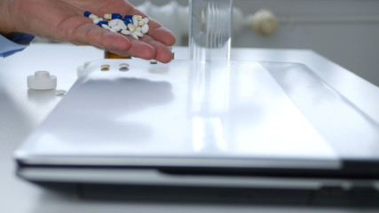 Image with a Man Taking Medical Pills Directly from a Laptop
