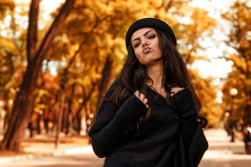 Beautiful curly woman in black hat standing on the background of colorful autumn leaves. space for text