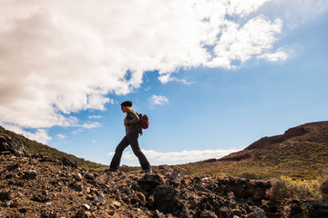 Expedition concept with woman walking on the rocks in trekking activity - outdoor leisure active people - scenic place with curved mountains horizon and blue sky with clouds