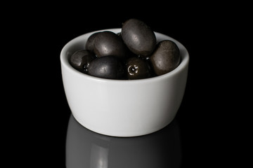 Lot of whole canned black olive in white sauce bowl isolated on black glass
