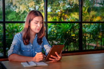 Beautiful Asian businesswoman who uses a tablet in the coffee shop to contact customers and check emails. Business concept