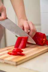 Chef slicing red fresh paprika along length on a bamboo board