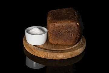 One whole fresh baked dark bread on bamboo plate with pinch of salt isolated on black glass