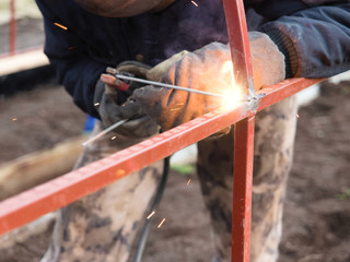 A qualified welder in protective gloves welds a metal structure using electric arc welding. Selective focus