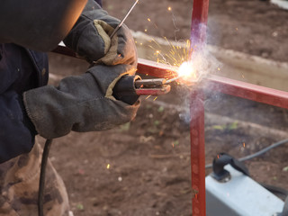 A craftsman in a protectives gloves, welds a metal structure using electric arc welding