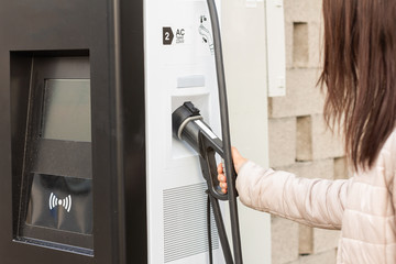 Woman use electrical fast charger to hybrid automobiles. High technology charger for green way of driving PHEV. Ecology friendly charger. New generation of environmental friendly green petrol station.