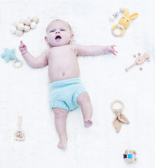 Portrait of displeased little baby lying on blanket with toys. Above view of baby boy wearing blue diaper resting in bed. Newborn child, childhood, healthy child