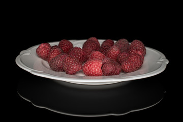 Lot of whole fresh crimson raspberry on white plate isolated on black glass