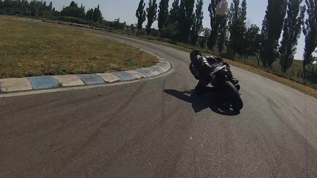 ZAPORIZHIA, UKRAINE - JUNE 17, 2019: black motorcyclist on a bike on a race track turns in a circle, bending his knee low to the asphalt. Summer, bright, sun, day, grass, trees, circle, race