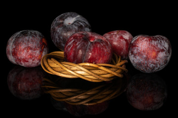 Group of five whole fresh red plum in wiker nest isolated on black glass
