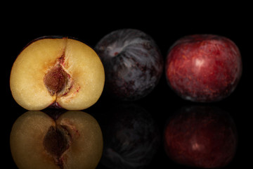 Group of two whole one half of fresh red plum isolated on black glass