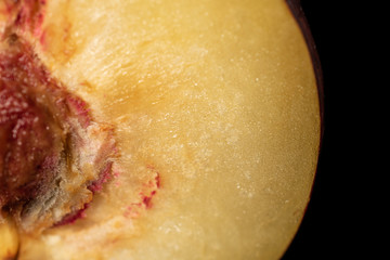 One half of ripened fresh red plum isolated on black glass