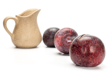 Group of three whole fresh red plum with ceramic jug isolated on white background