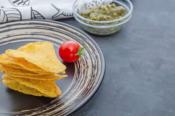 nachos on a black plate with guacamole and cherry tomato sauce in the background.