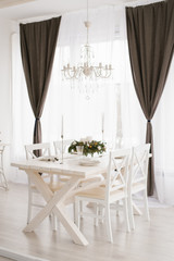 Bright dining set: a table with chairs in the bright living room is opposite the window, above the table hangs a white chandelier