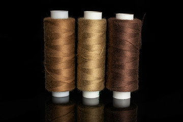Group of three whole haberdashery item standing thread spools isolated on black glass